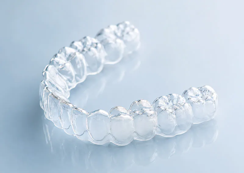 A clear Invisalign aligner tray on a reflective surface